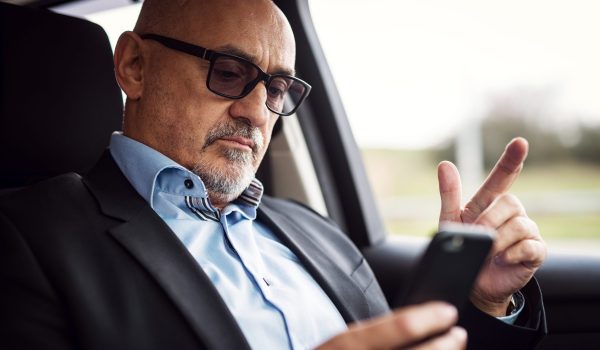 Mature serious businessman is sitting in his car and looking curious in his phone.
